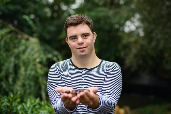 Portrait of down syndrome adult man standing outdoors at green background, holding nuts in hands.