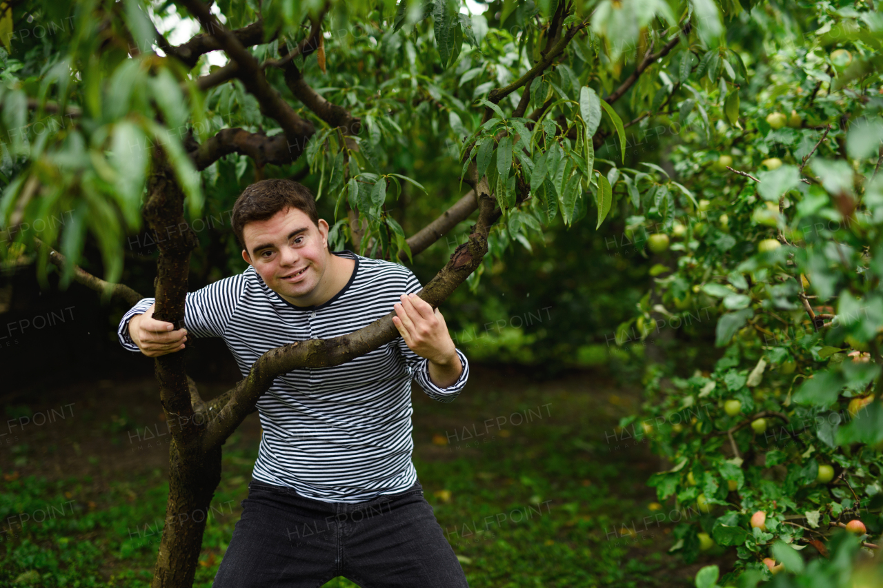 Front view portrait of down syndrome adult man standing outdoors under tree.