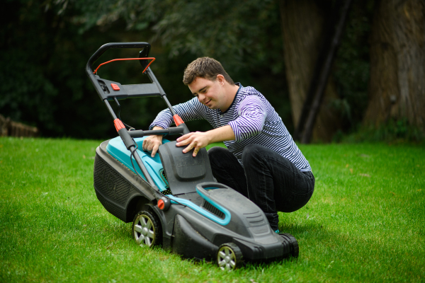 Portrait of down syndrome adult man mowing lawn outdoors in backyard, helping with housework concept.