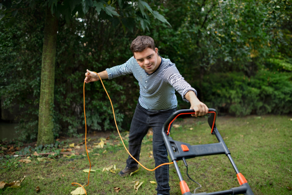 Portrait of down syndrome adult man mowing lawn outdoors in backyard, helping with housework concept.