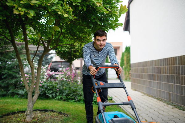 Portrait of down syndrome adult man mowing lawn outdoors in backyard, helping with housework concept.