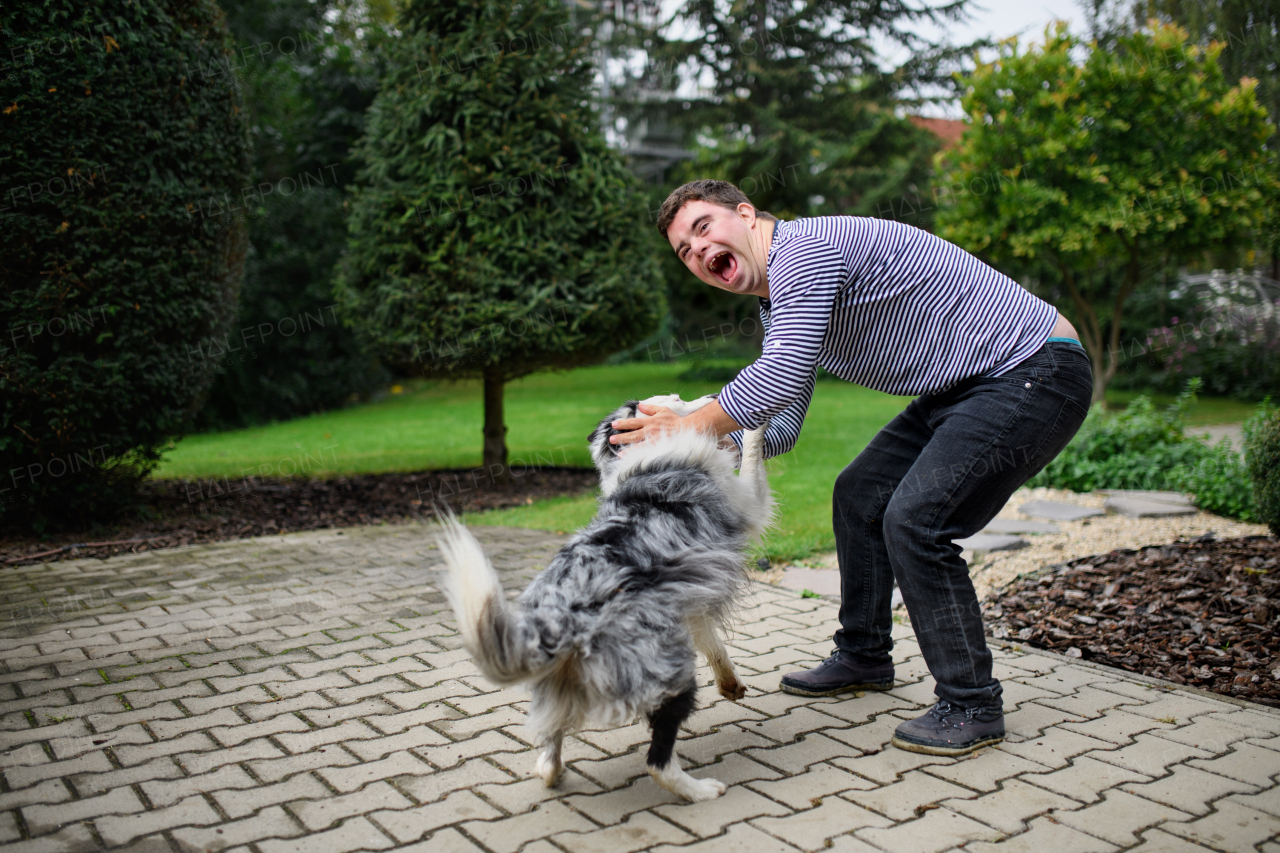 Portrait of cheerful down syndrome adult man playing with dog pet outdoors in backyard.