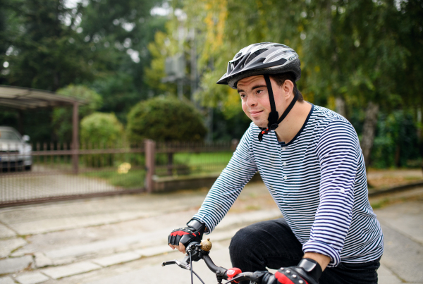 A portrait of down syndrome adult man with bicycle cycling outdoors on street.