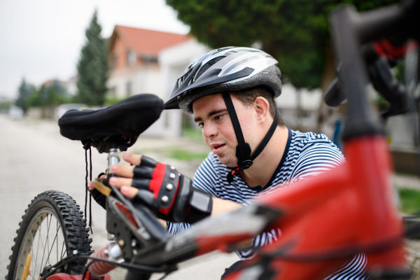 Portrait of down syndrome adult man with bicycle and helmet standing outdoors on street, repairing.