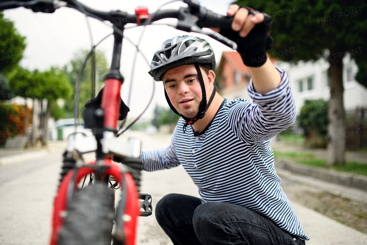 Portrait of down syndrome adult man with bicycle and helmet standing outdoors on street.