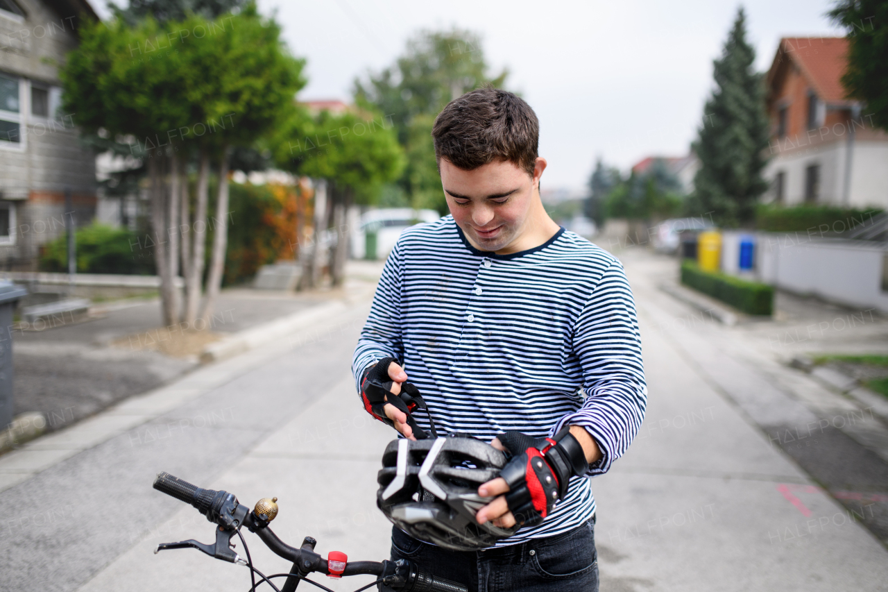 Portrait of down syndrome adult man with bicycle and helmet standing outdoors on street.