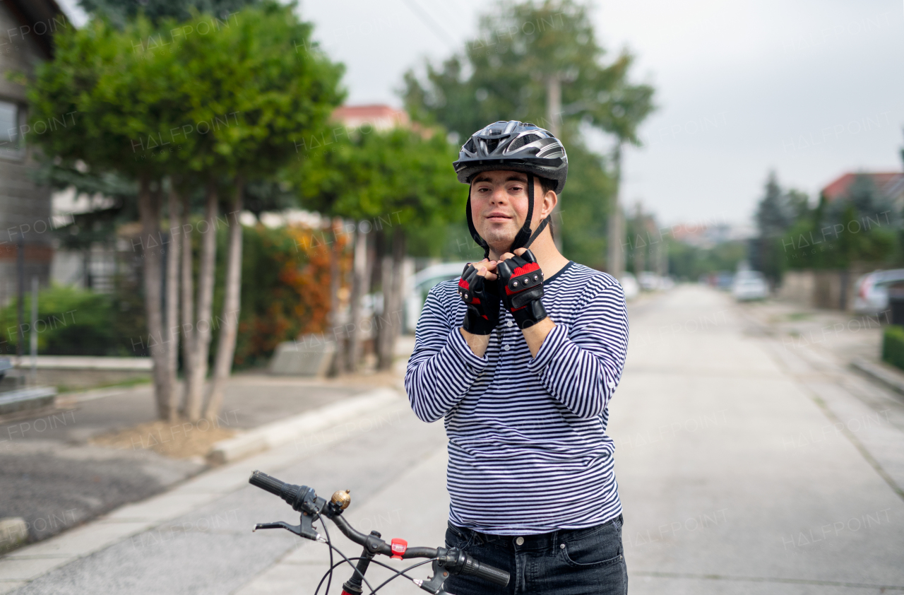 Portrait of down syndrome adult man with bicycle standing outdoors on street, looking at camera.