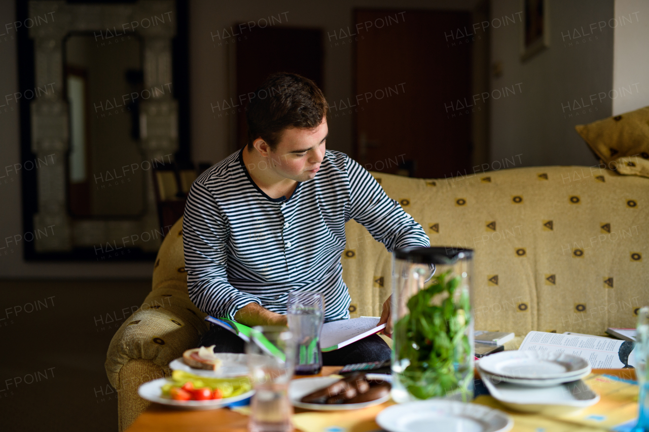 Portrait of down syndrome adult man sitting indoors at home, resting on sofa.