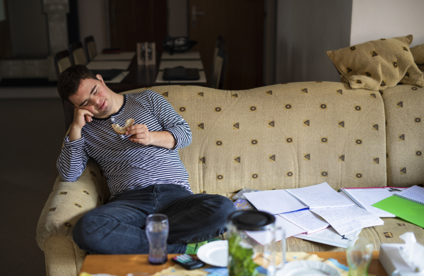 Portrait of down syndrome adult man sitting indoors at home, resting on sofa.