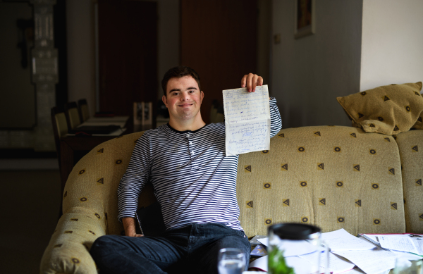 Portrait of down syndrome adult man sitting indoors at home, writing.