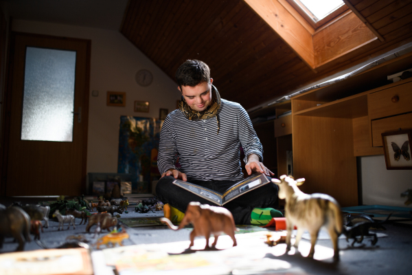 Down syndrome adult man sitting indoors in bedroom at home, playing with abd studying about animals.