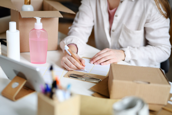 An unrecognizable woman dropshipper working at home, packing parcels. Coronavirus concept.