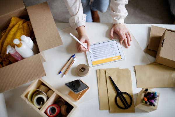 Unrecognizable young woman dropshipper working at home, using tablet. Coronavirus concept.