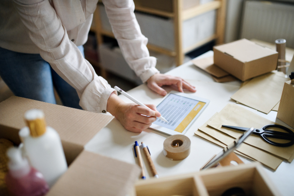 Unrecognizable young woman dropshipper working at home, using tablet. Coronavirus concept.