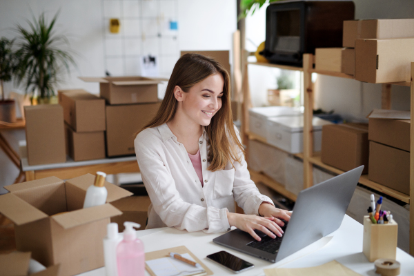 Young woman dropshipper with laptop working at home, processing orders. Coronavirus concept.