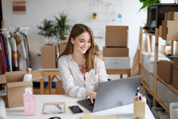 Young woman dropshipper with laptop working at home, processing orders. Coronavirus concept.