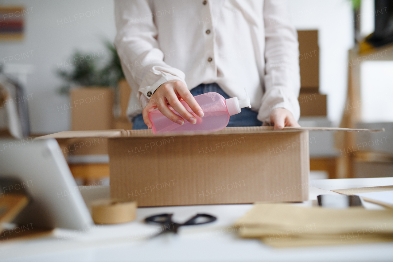 Midsection of unrecognizable woman dropshipper working at home, packing parcels. Coronavirus concept.