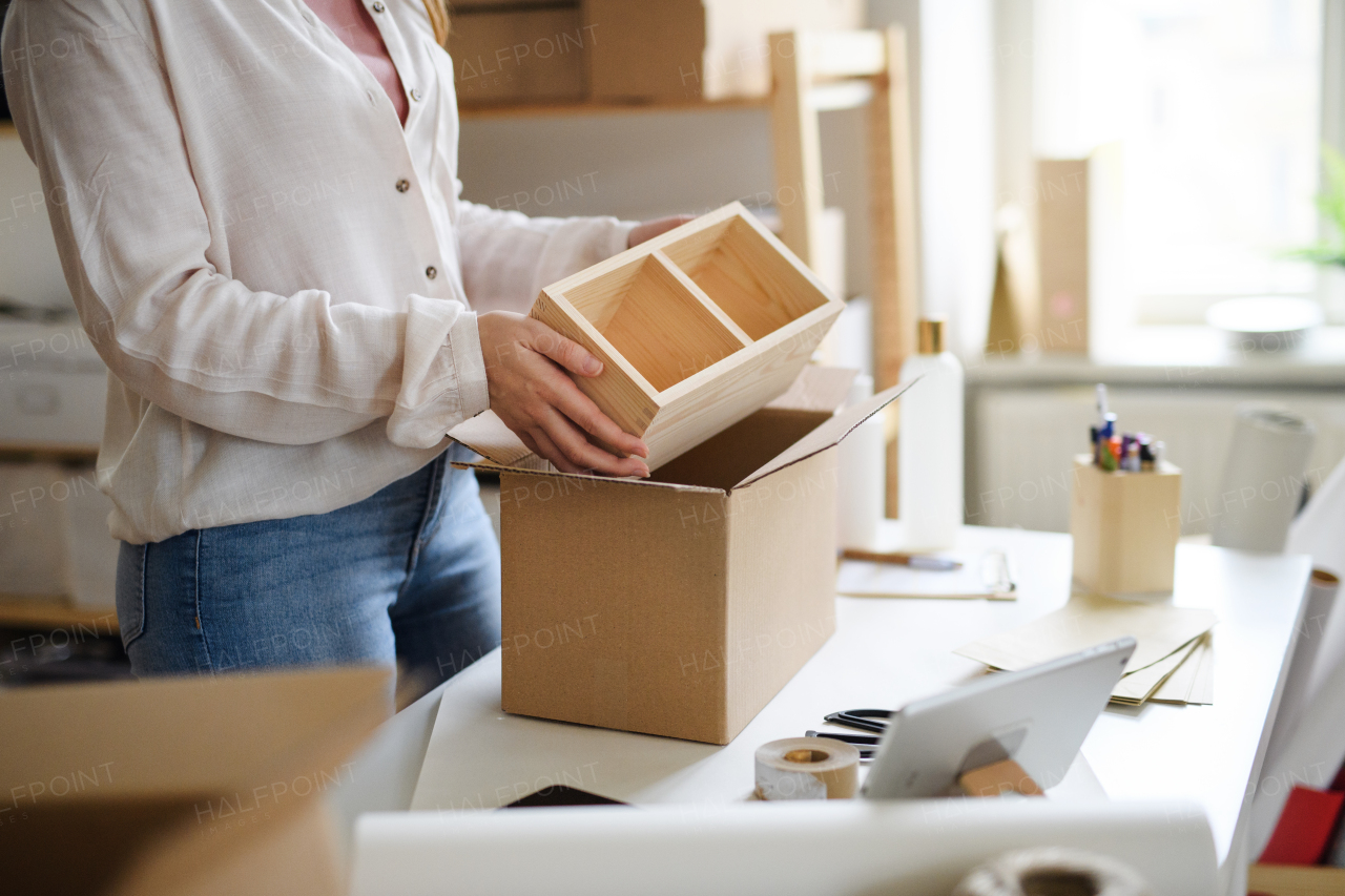 An unrecognizable woman dropshipper working at home, packing parcels. Coronavirus concept.