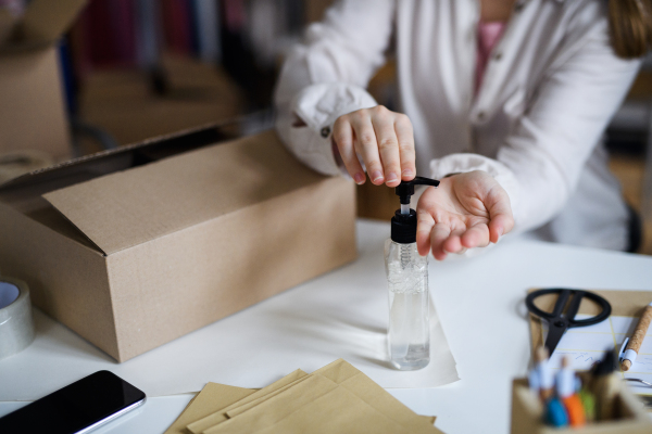 Midsection of unrecognizable woman dropshipper working at home, disinfecting hands. Coronavirus concept.