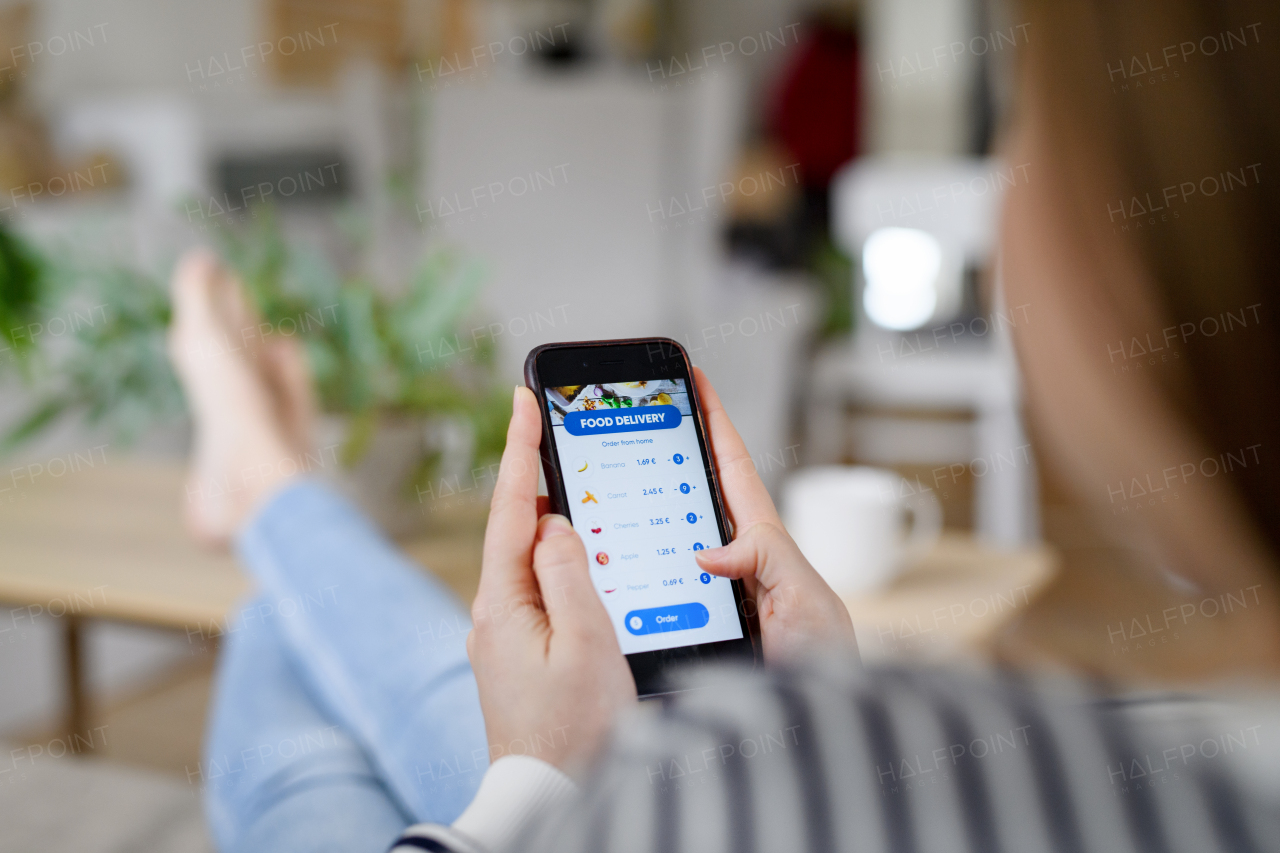 Midsection of unrecognizable woman with smartphone ordering food at home, coronavirus and food delivery concept.