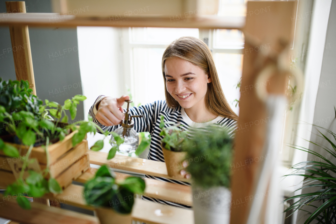 Happy woman spraying plants with water working at home, plant care concept.