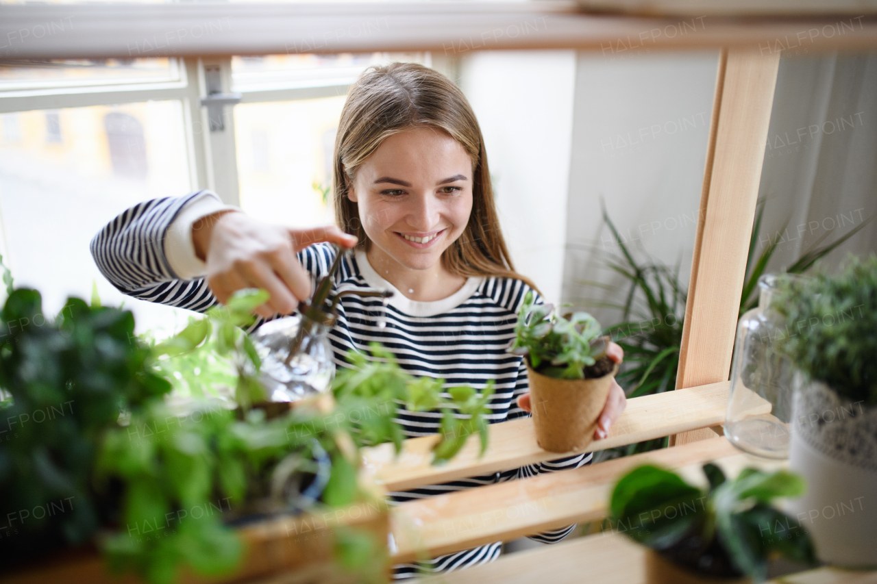 Happy woman spraying plants with water working at home, plant care concept.