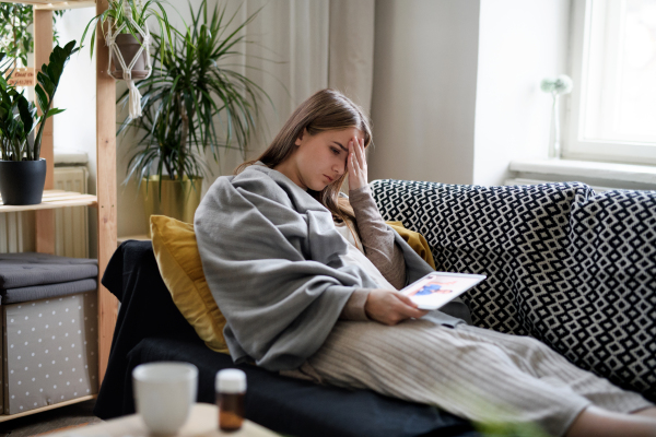 An ill young woman having video call with doctor on tablet at home, online consultation concept.