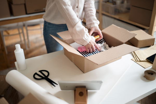 An unrecognizable woman dropshipper working at home, packing parcels. Coronavirus concept.