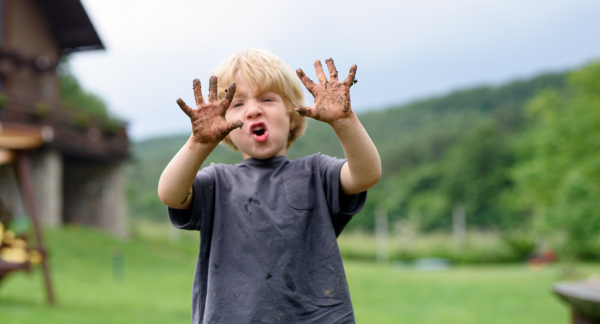 Small boy showing dirty hands standing in vegetable garden, sustainable lifestyle.