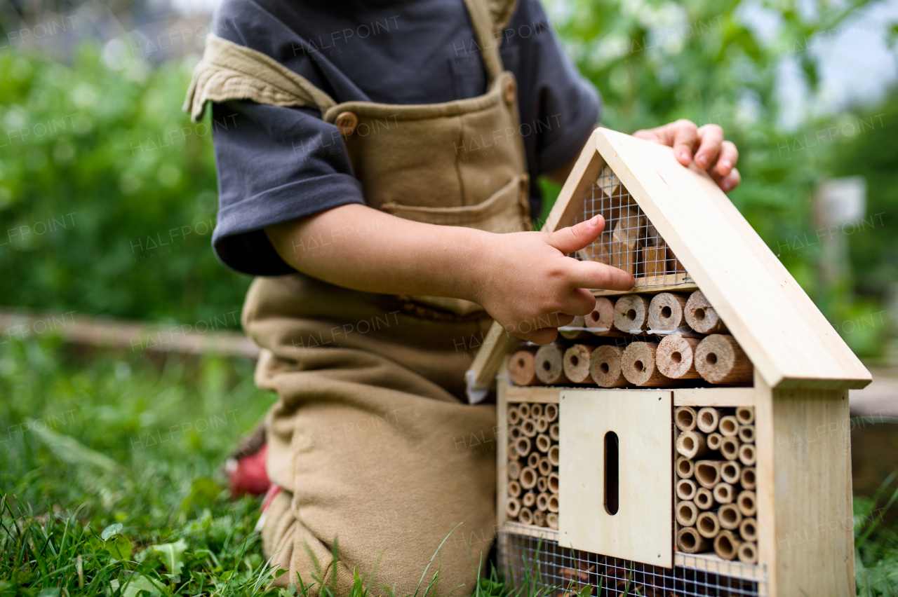 Obscured small child playing with bug and insect hotel in garden, midsection of sustainable lifestyle.