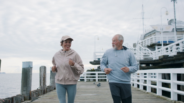 Happy senior couple running outdoors on pier by sea at the morning.