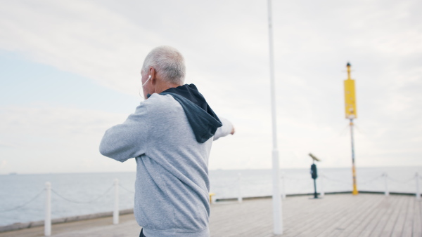 A senior man outdoors on pier by sea at the morning, stretching after run.