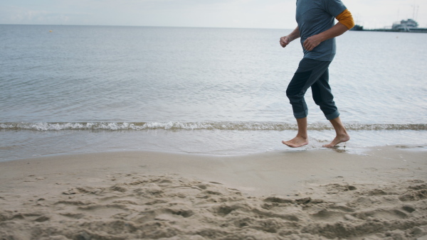 Side view of unrecognizable senior couple running outdoors on beach by sea at the morning.