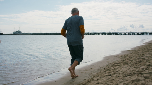 A rear view of senior couple running outdoors on beach by sea at the morning.