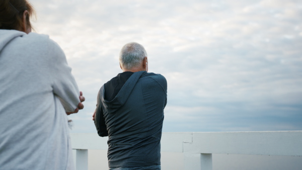 A happy senior couple outdoors on pier by sea at the morning, stretching after run.