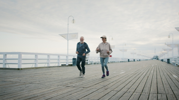 Happy senior couple running outdoors on pier by sea at the morning.