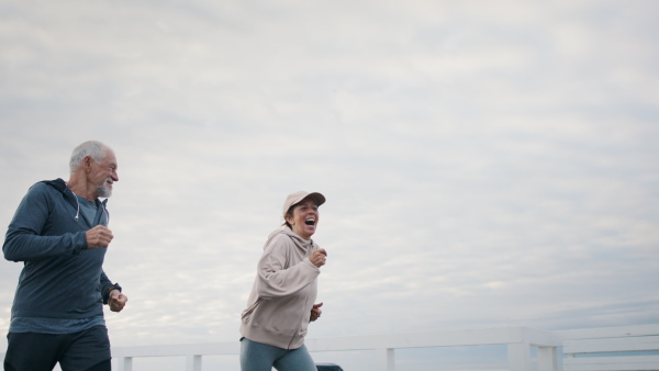 Happy senior couple running outdoors on pier by sea at the morning.