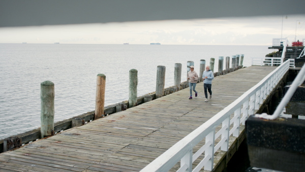 Top view of happy senior couple running outdoors on pier by sea at the morning.