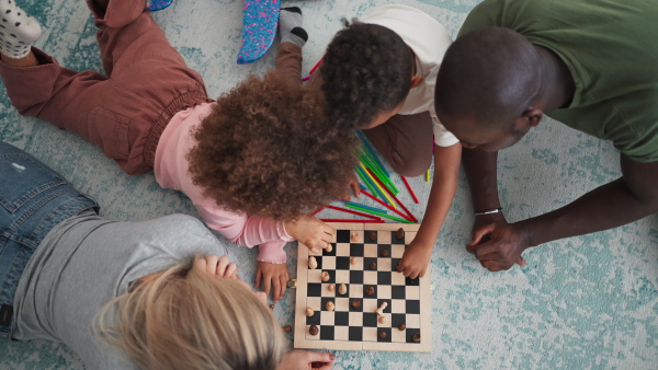 A top view of young multiracial family lying on floor and playing chess at home.