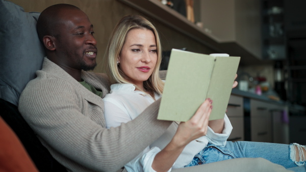 A mid adult biracial couple in love sitting and reading book together at home.