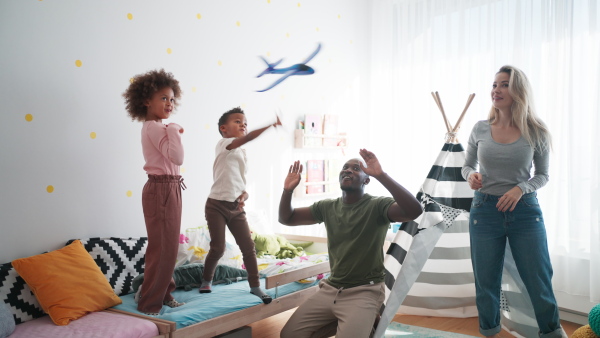 Two little multiracial kids with a mother and father playing with toy planes at home.