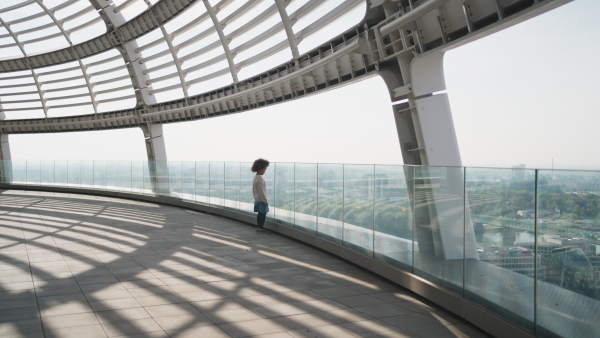 A little multiracial girl with afro hairstyle standing on bridge and looking at city view outdoors.