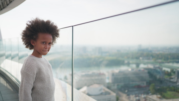 A little multiracial girl with afro hairstyle standing on bridge and looking at city view outdoors.