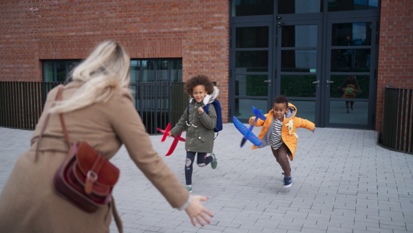 Happy little multiracial sbilings running to their mother waiting for them after a school outdoors in street.