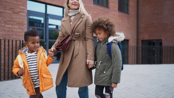 A happy mother taking children home from school, walking outdoors in street, multiracial family.