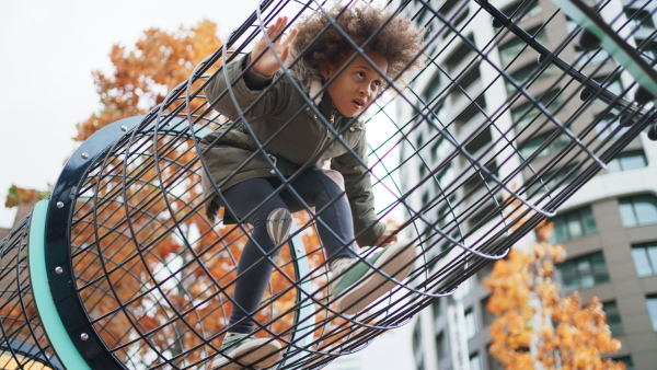 A happy multiracial girl climbing through tunnel outdoors at playground.