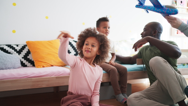 Two little multiracial kids with a mother and father playing with toy planes at home.