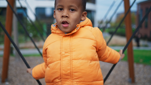 A happy multiracial boy playing outdoors at playground in winter.