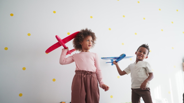 Two little african american kids playing with the toy planes at home.