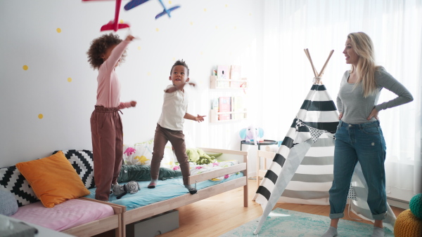 Two little multiracial kids with a mother playing with toy planes at home.